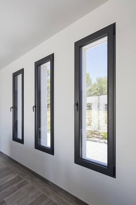 Trois fenêtres aluminium noir hautes et étroites avec poignées, alignées sur un mur blanc
